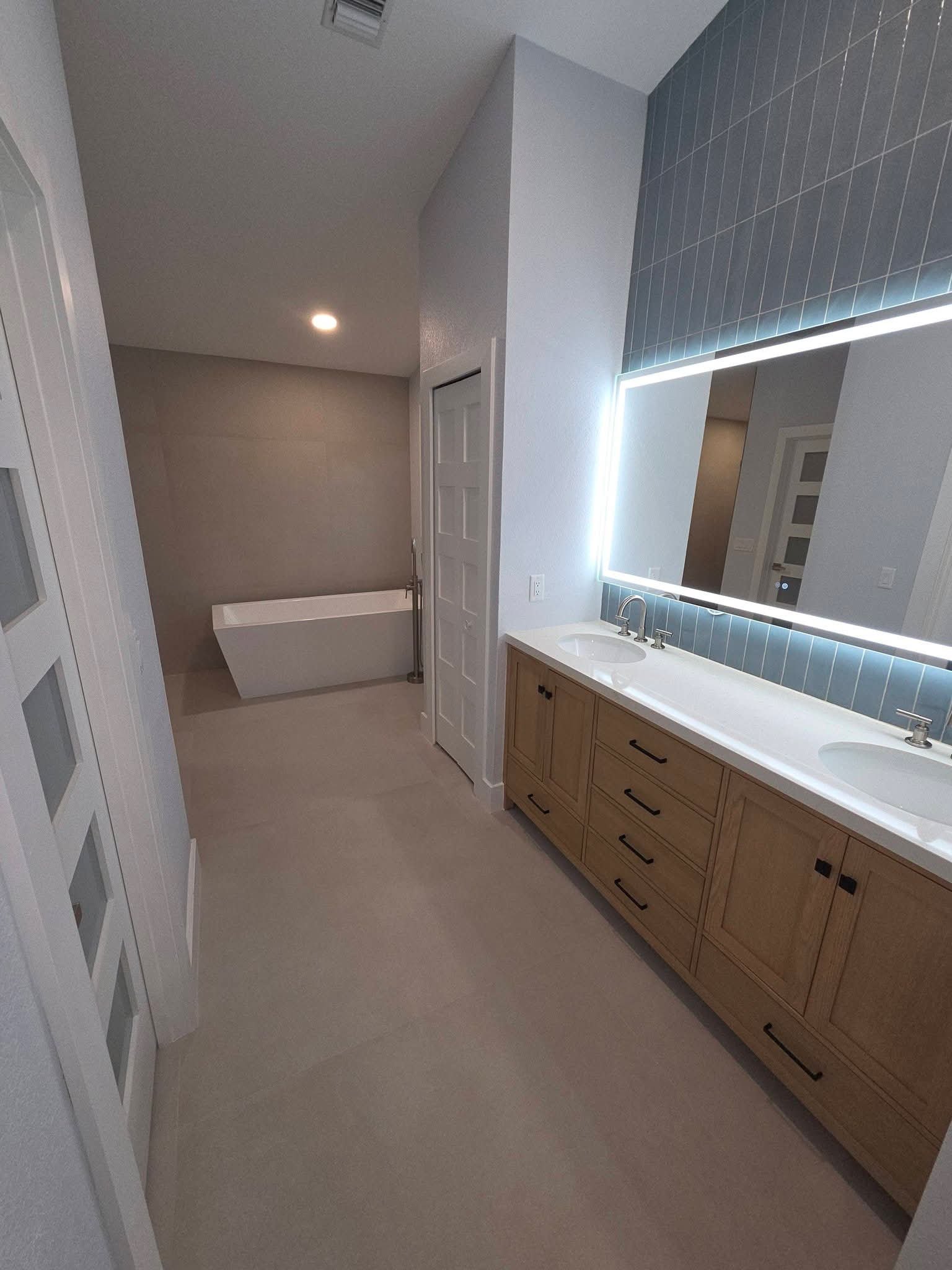 Master bathroom with double wood vanity, lit mirror and freestanding tub